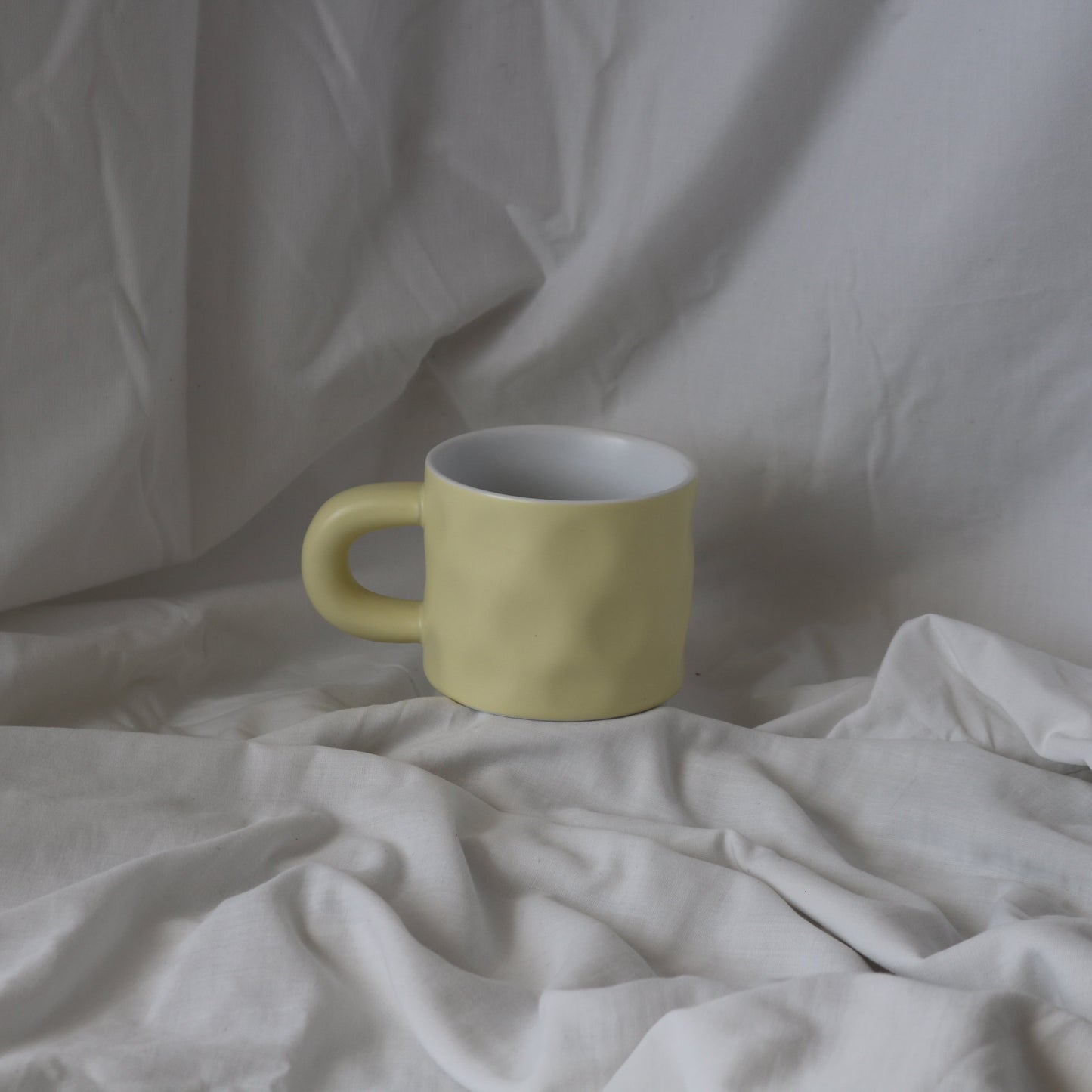 Pale yellow ceramic mug with dimpled texture, featuring a rounded handle.