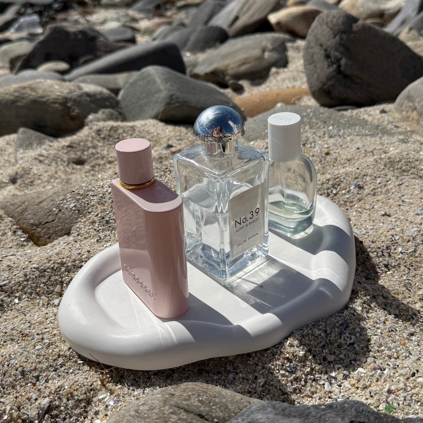 Organic-shaped handmade white tray made from eco resin, styled on beach sand with natural stones and perfume bottles.