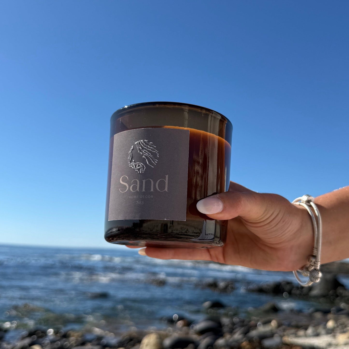 Large scented soy candle in an amber glass jar with a beach setting as the background.