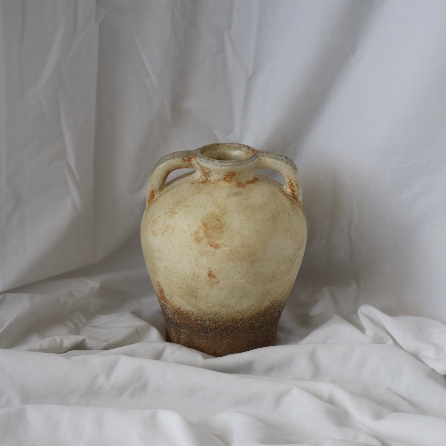 Rustic Mediterranean round vase with a dark brown bottom and rustic beige top half. With a white linen back drop.