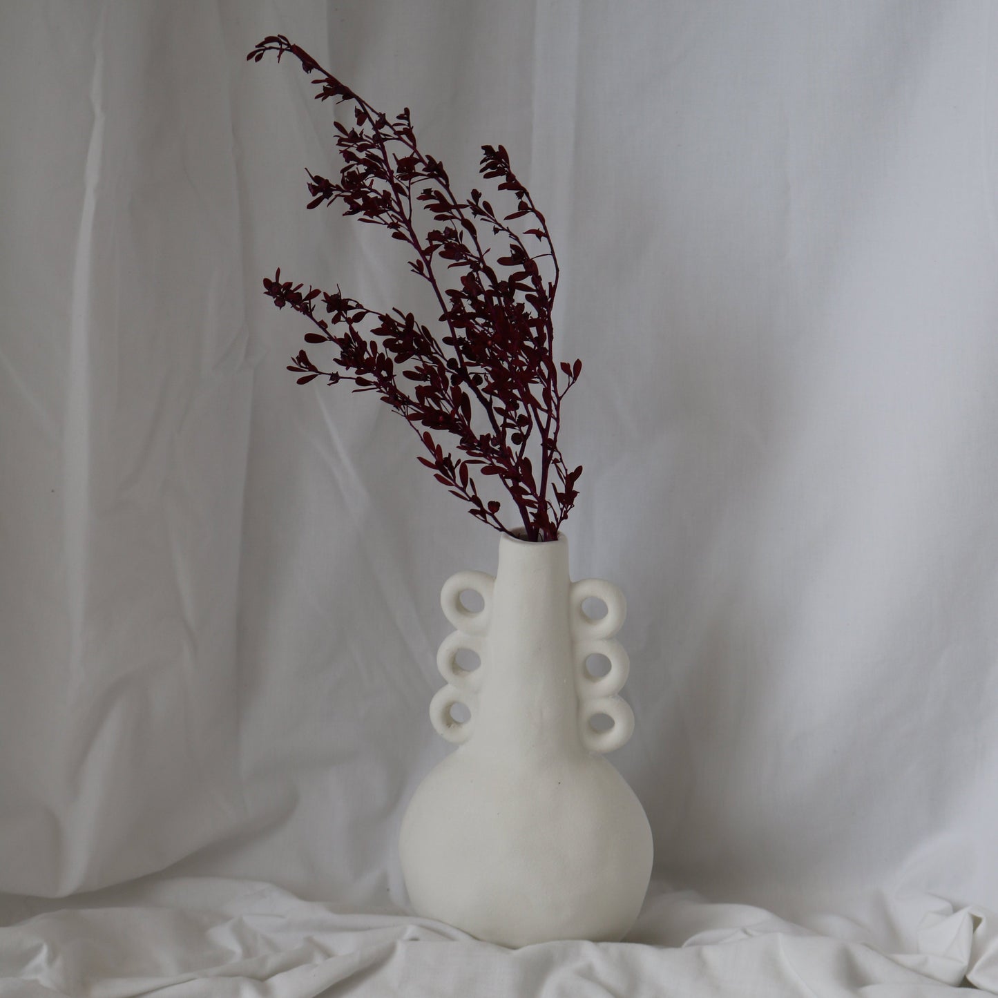 White tall textured vase with 3 ears on each side with foliage for styling.
