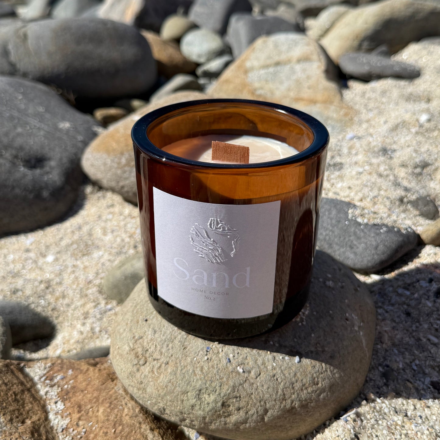 Large scented soy candle in an amber glass jar with a beach setting as the background.