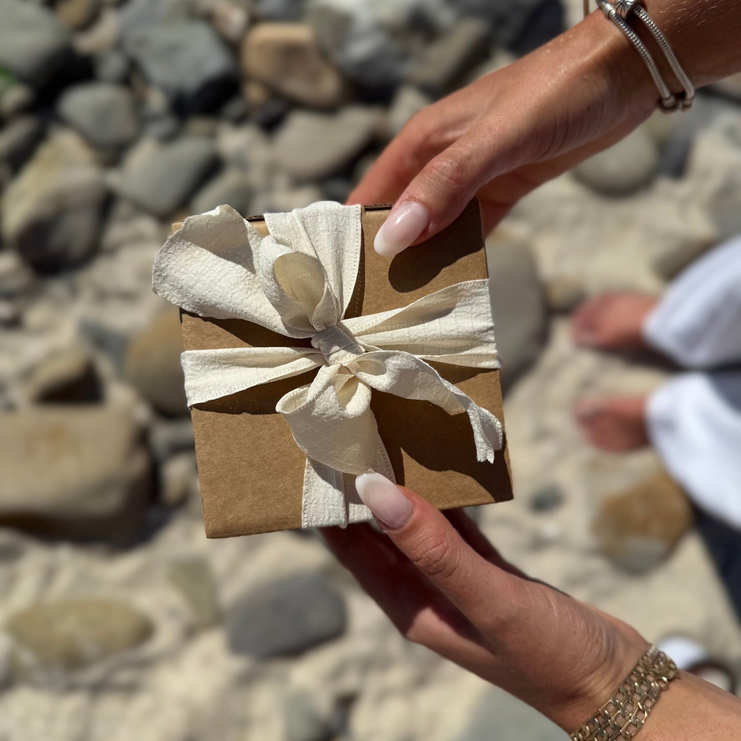Large scented soy candle in its beautiful packaging wrapped in ribbon photographed on the beach.