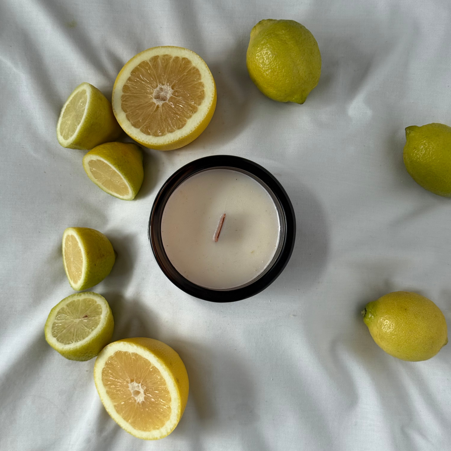 Candle surrounded by lemons on a white fabric background
