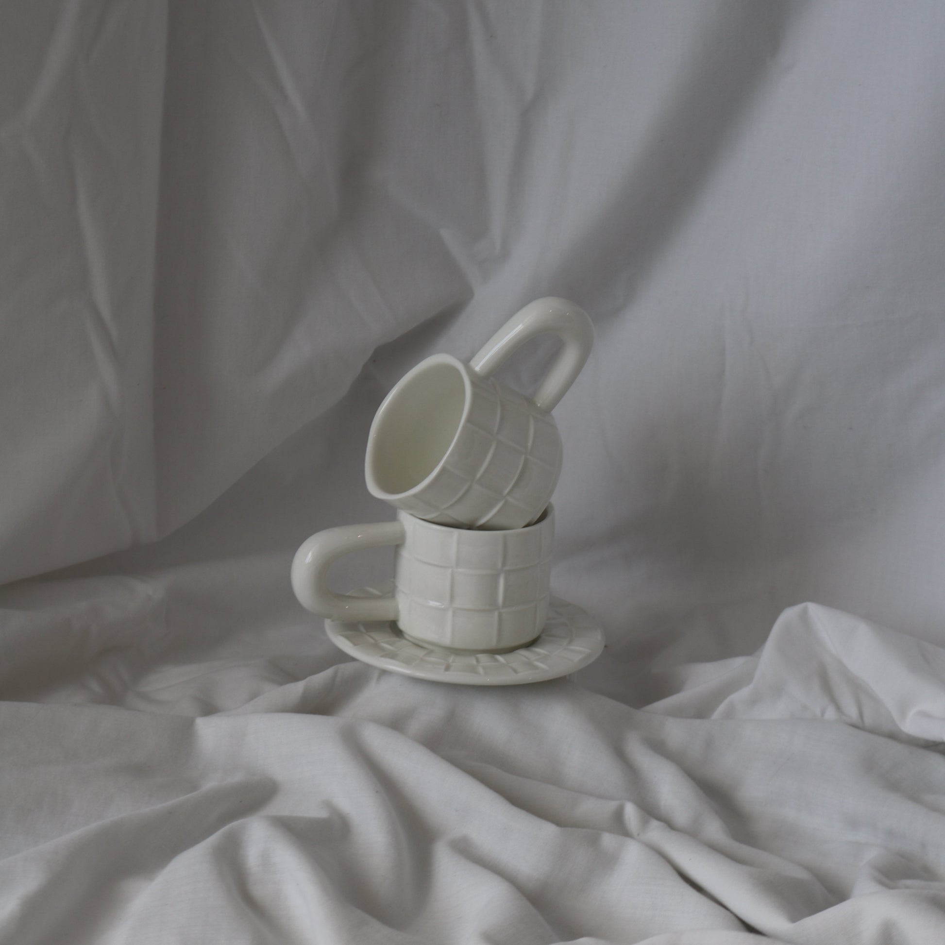 White ceramic cup with a grid texture, accompanied by a matching textured saucer.