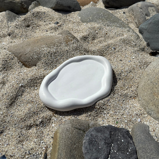 Organic-shaped handmade white tray made from eco resin, styled on beach sand with natural stones.

