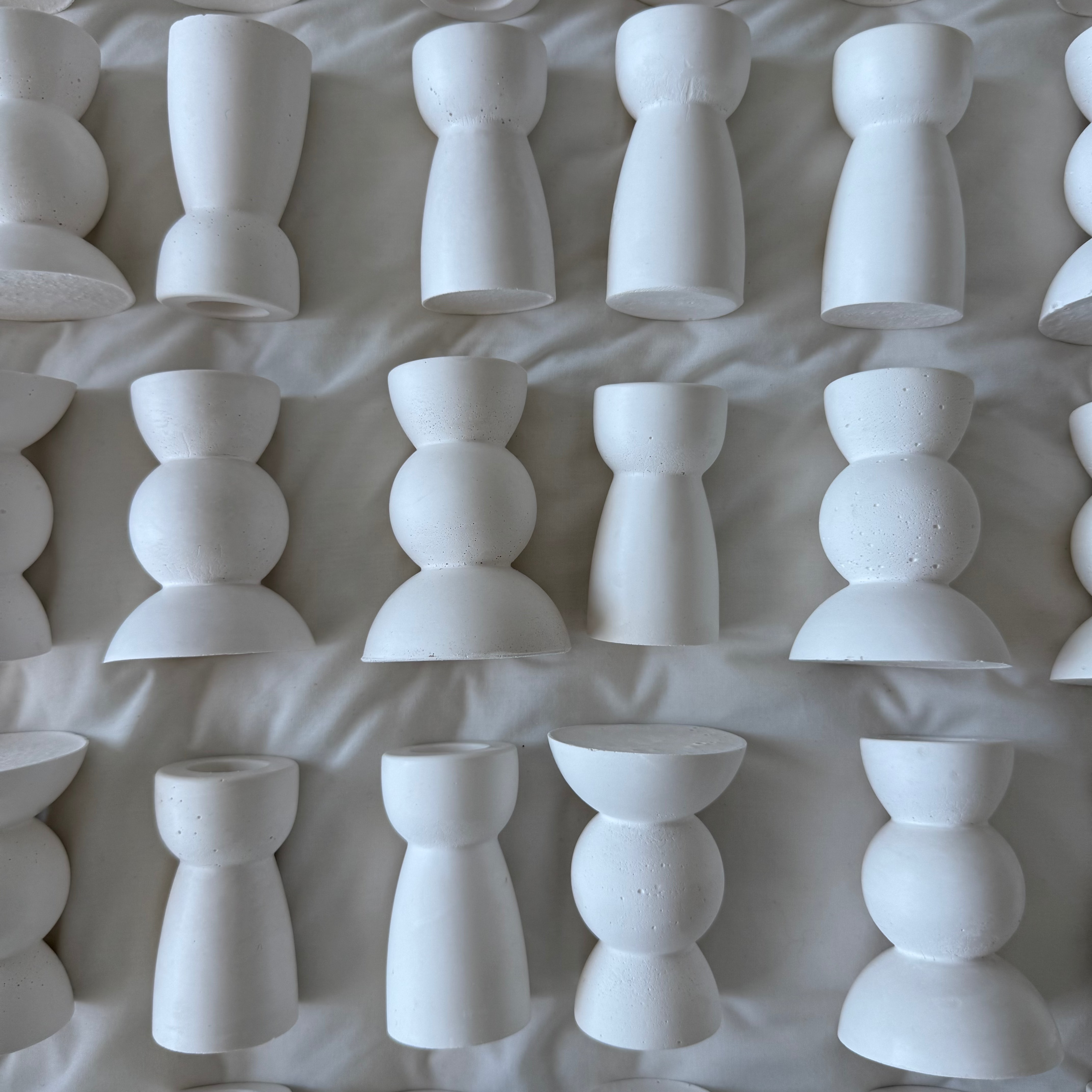 A collection of white ceramic candle holders arranged in rows on a white fabric background.