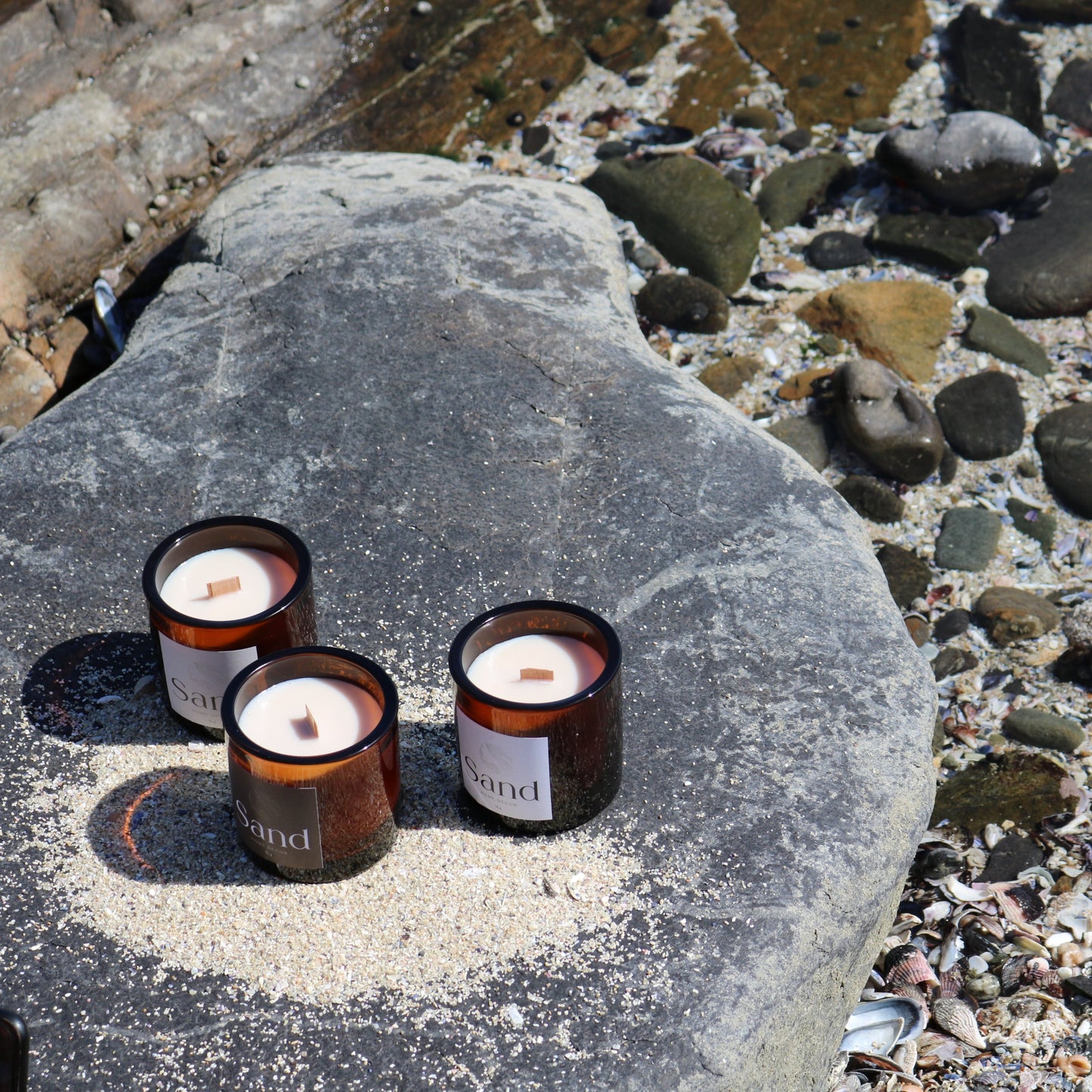 Scented large luxury soy candles in an amber glass jar sitting on a rock with a rocky background. 