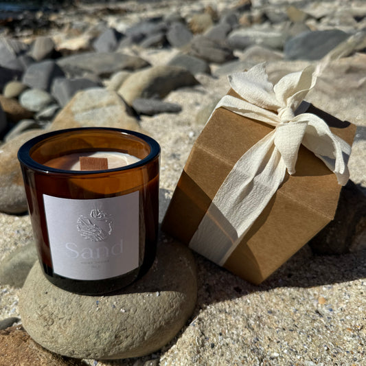 Large scented soy candle in an amber glass jar with a beach setting as the background.               