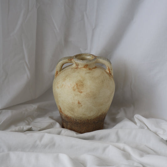 Rustic Mediterranean round vase with a dark brown bottom and rustic beige top half. With a white linen back drop. 