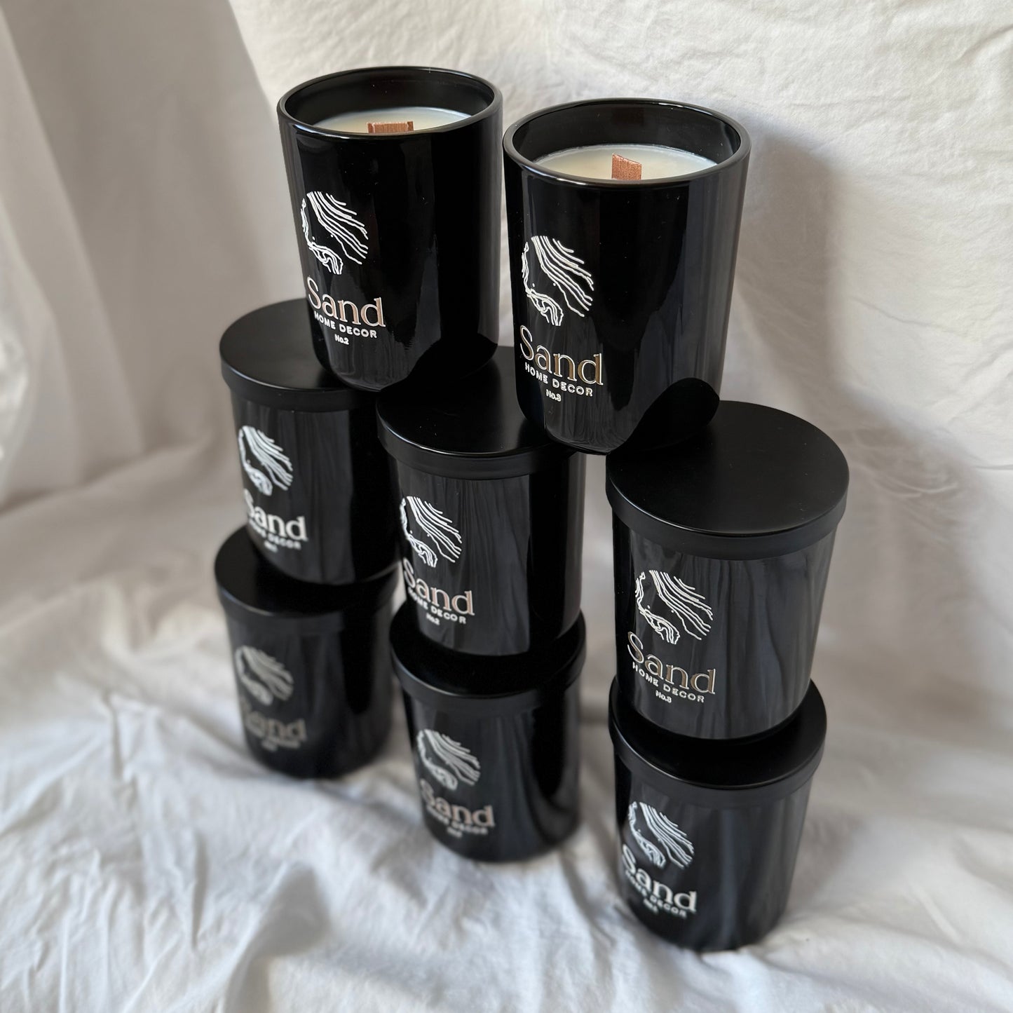Stack of black candles with 'Sand' branding on a white fabric background