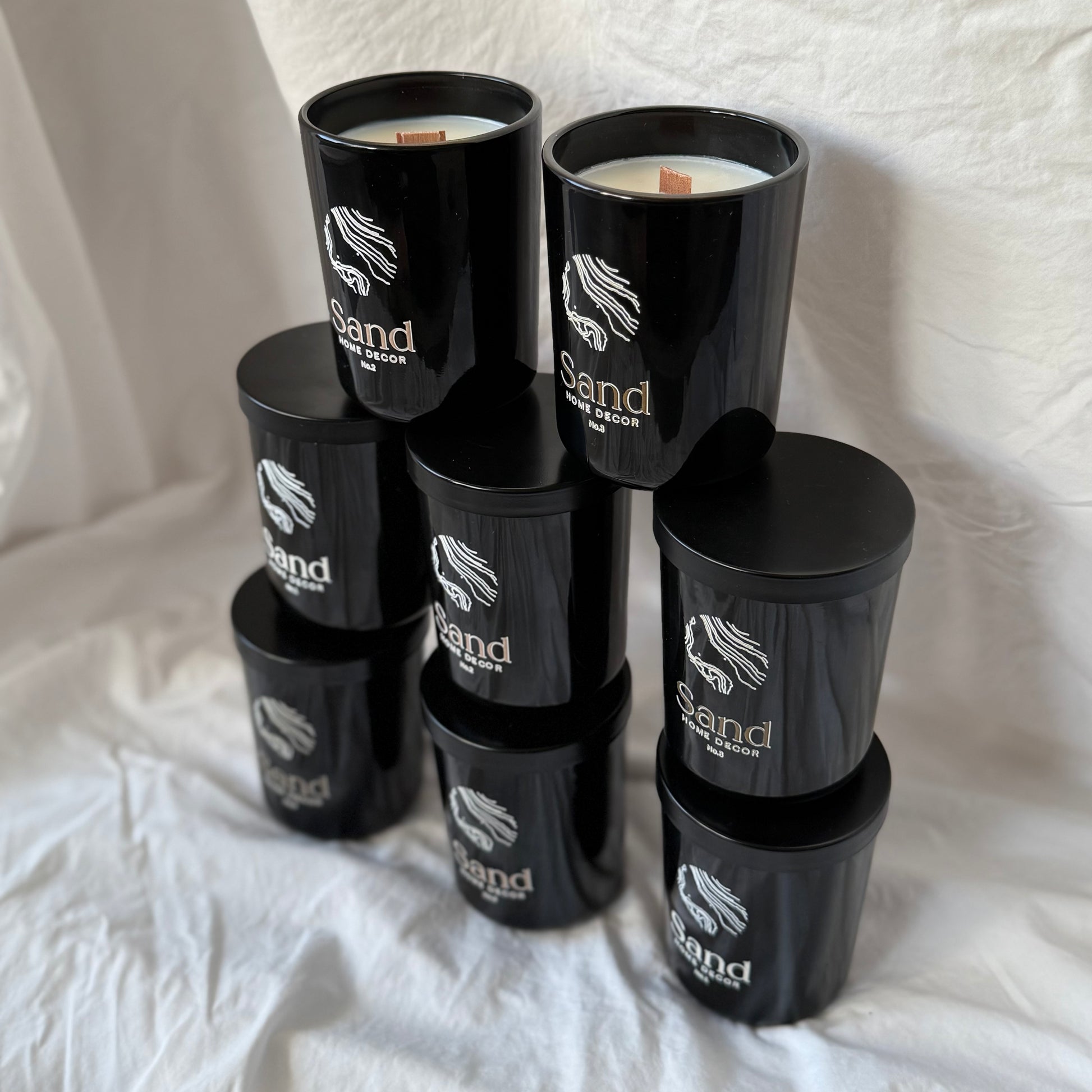 Stack of black candles with 'Sand' branding on a white fabric background