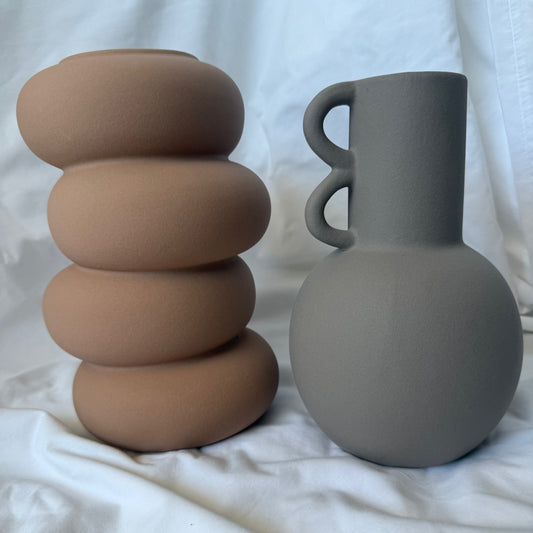 Contemporary ceramic vase with stacked pebble-inspired design in a smooth warm terracotta  finish, placed on soft white fabric.