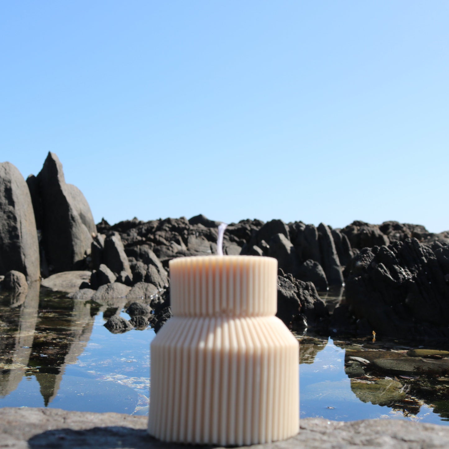 A decorative tiered candle in ivory. The scene features a natural rocky backdrop.