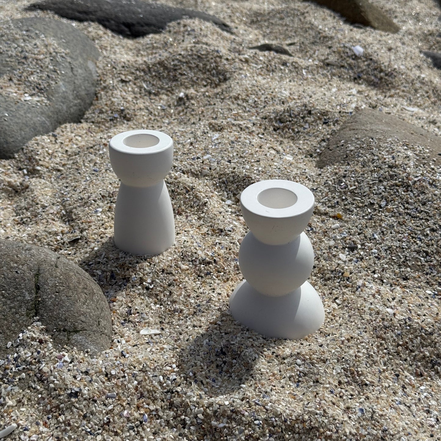 Two modern white candle holders made from eco resin, placed on a sandy beach in Cape Town.