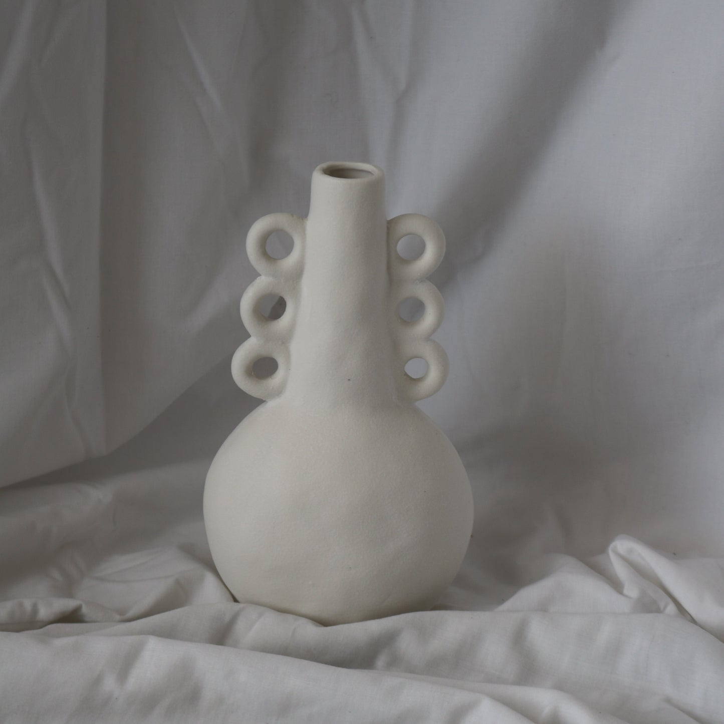 white textured tall vase with three round ears on each side of the neck. 