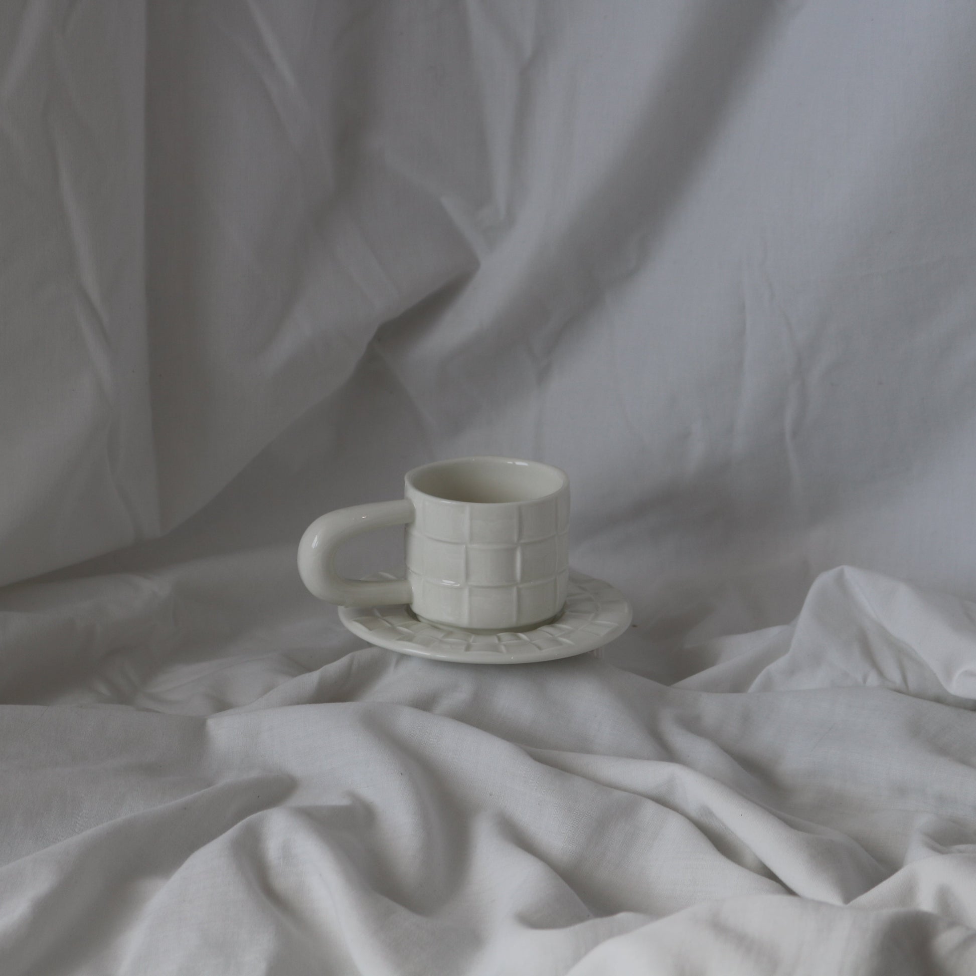 White ceramic cup with a grid texture, accompanied by a matching textured saucer.