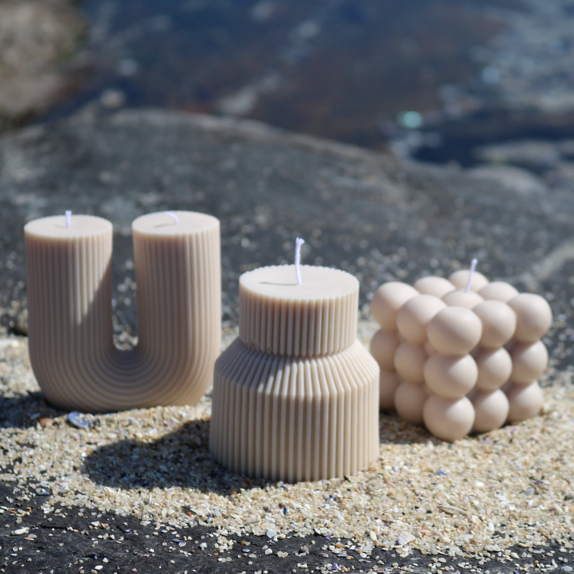 Image of three scented, ivory coloured handmade candles next to each other with a rocky background.