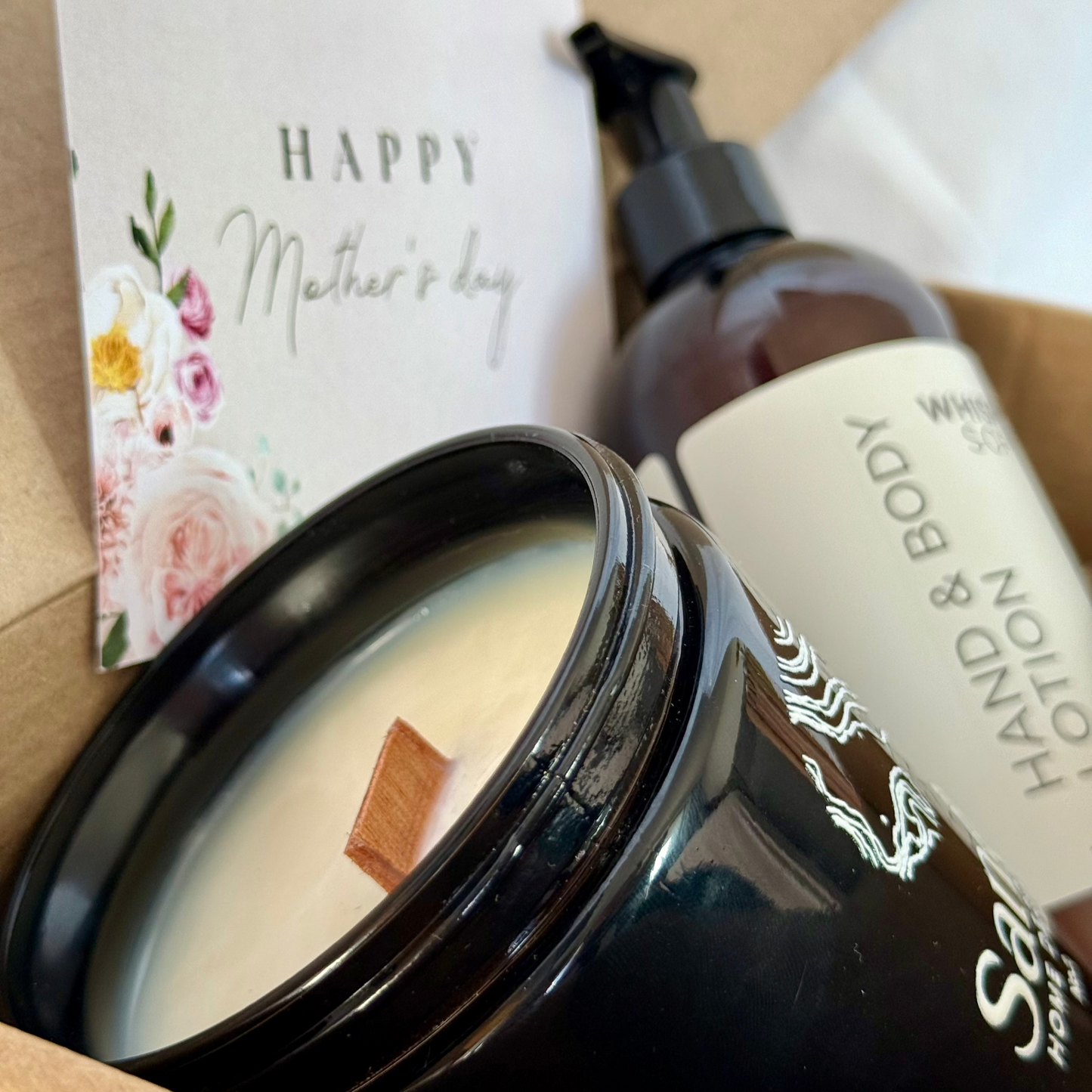 zoomed up image of a gift box with a handmade soy candle with a wooden wick, hand cream and a happy mothers day  note.