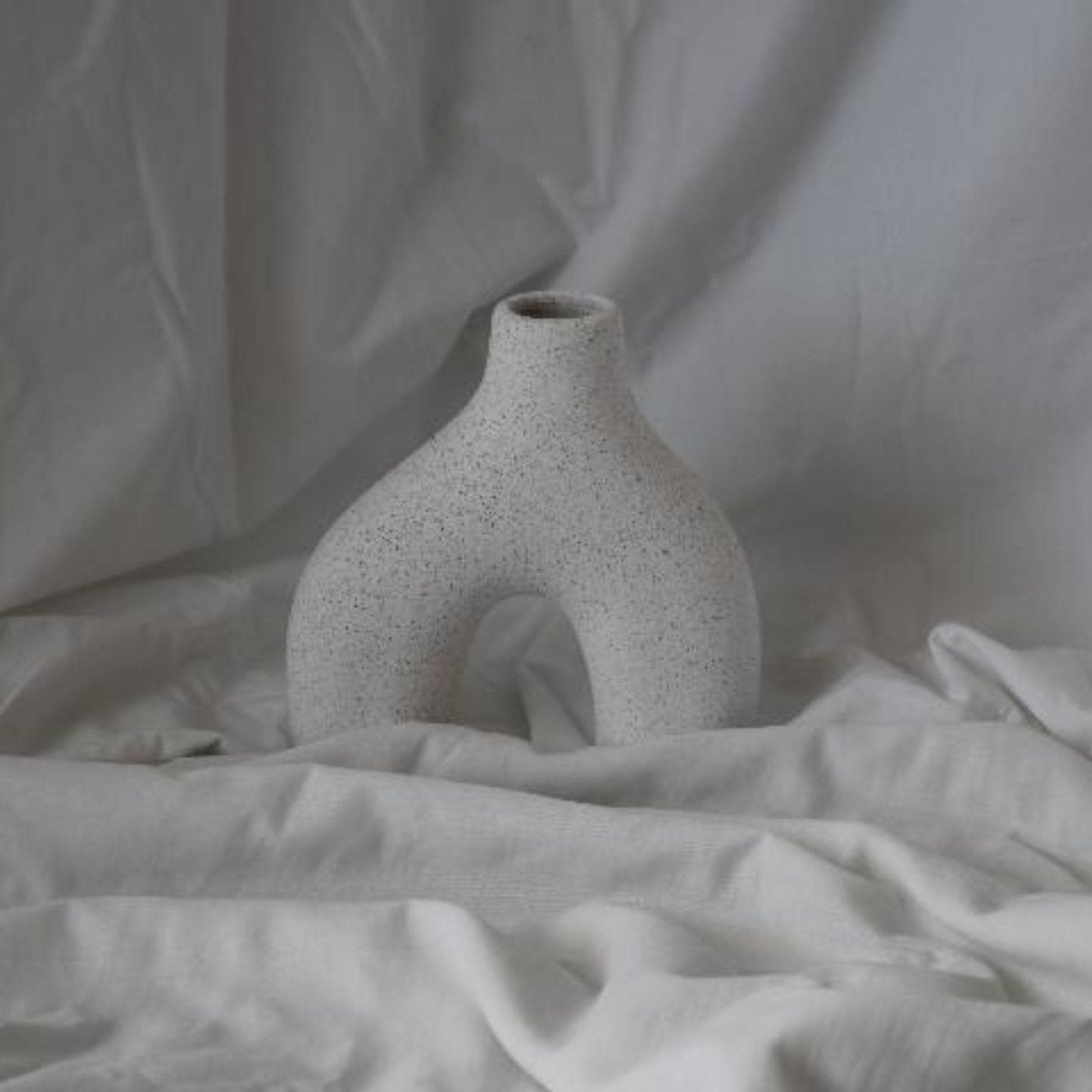 Minimalist white ceramic vase with a modern, sculptural design and speckled texture, perfect for contemporary home decor or as a statement piece.