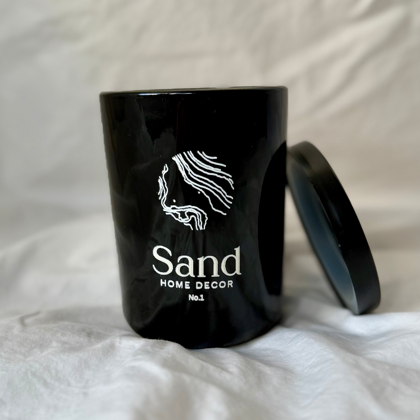 Black decorative container with 'Sand Home Decor' branding on a white fabric background
