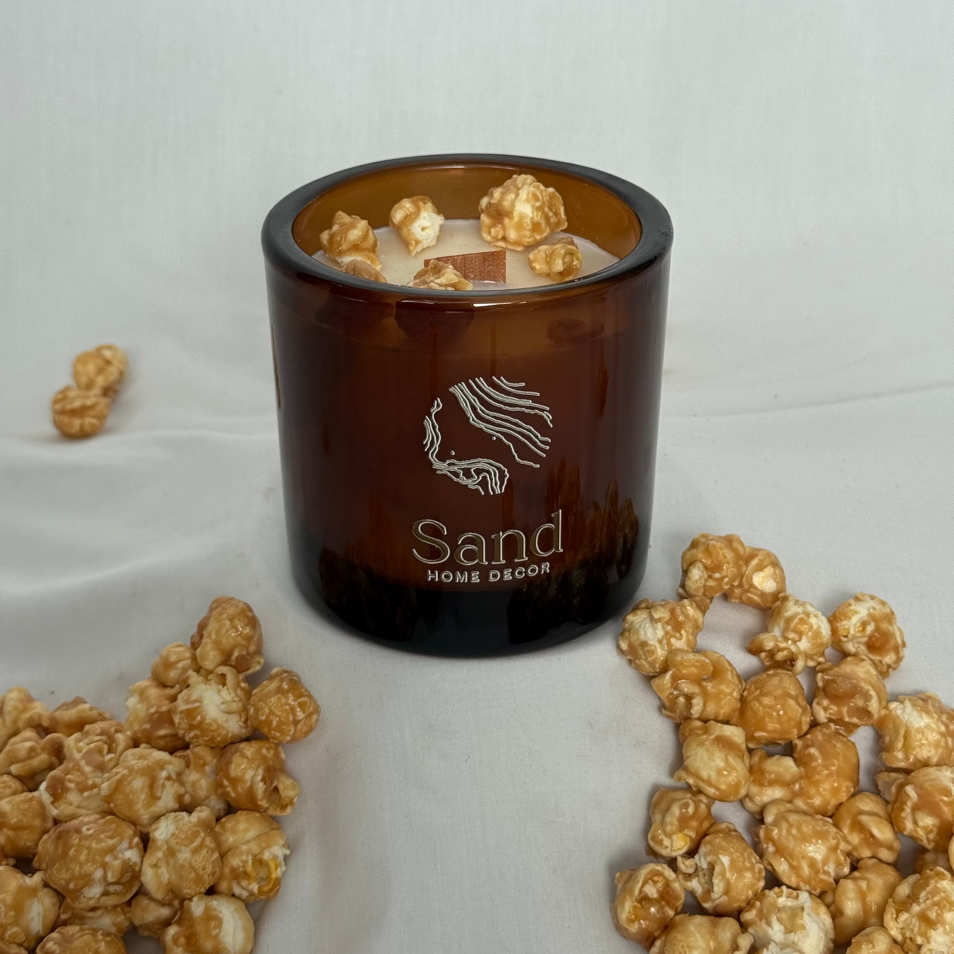 Brown candle with popcorn on a white surface, featuring 'Sand Home Decor' branding.