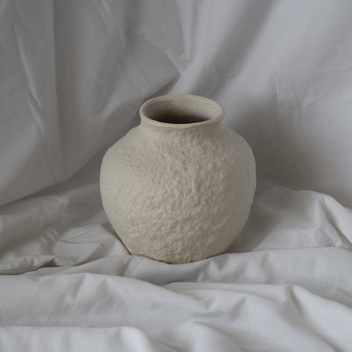 Textured white round vase with a white linen background.