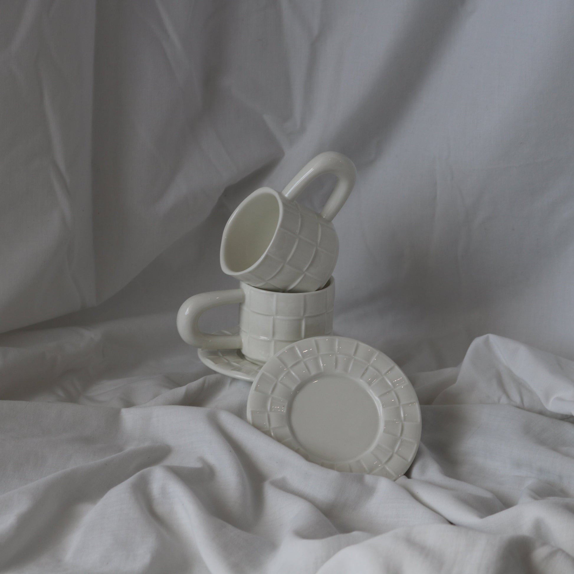 White ceramic cup with a grid texture, accompanied by a matching textured saucer.